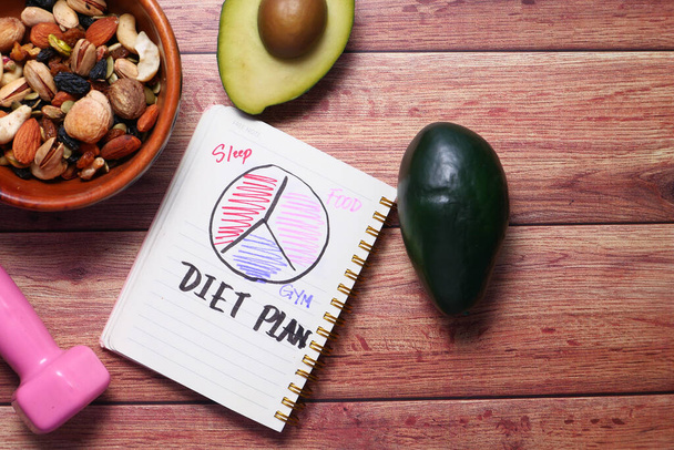 Diet plan with almond nut, dumbbells, avocado on table . - Photo, image