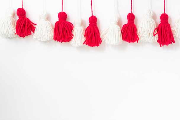 brushes from yarn of red and white color on a white background. Space for copy space. DIY yarn brushes. Garland. Garland of yarn. Pampushki from yarn. Children's creativity - Fotó, kép