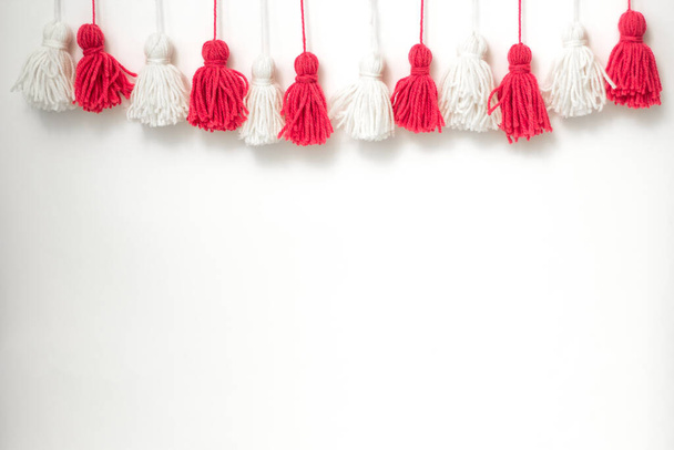 brushes from yarn of red and white color on a white background. Space for copy space. DIY yarn brushes. Garland. Garland of yarn. Pampushki from yarn. Children's creativity - 写真・画像