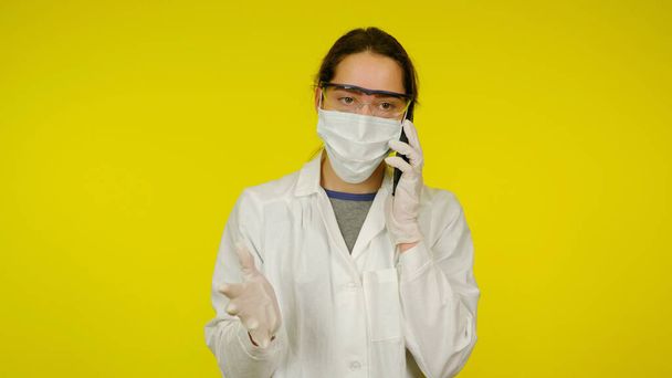Un médico joven con una máscara médica, gafas y guantes de látex está hablando por teléfono
 - Foto, imagen