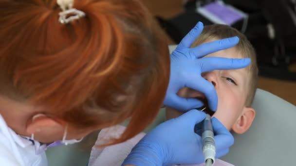 Маленький хлопчик сидить у стоматологічному кріслі. Мила дитина відкриває рот стоматологу. Доктор перевіряє зуби хлопчика
. - Кадри, відео
