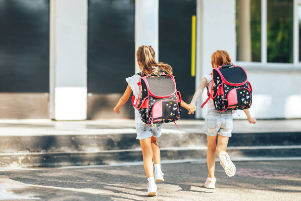 Two schoolgirls holding each others hands run to school, back to school, primary education of children - 写真・画像