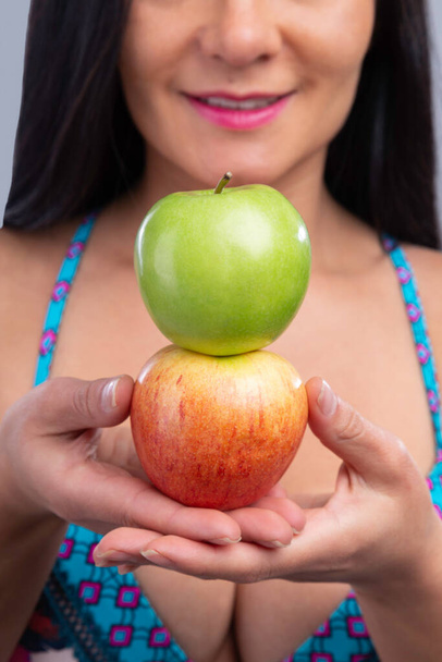 латиноамериканка держит два органических яблока красные и зеленые, улыбаясь - Фото, изображение