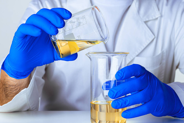 Scientist or doctor in blue gloves pouring some yellow liquid into a flask - Фото, зображення