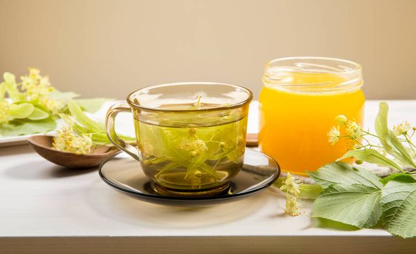 Tilia platyphyllos известна как крупнолистная липа травяной чай со свежесобранными цветами и банка меда с листьями деревьев и ветви с цветами для украшения на деревянном столе
. - Фото, изображение