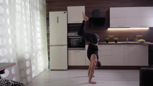 An athlete makes a rack on his hands at home in the background of a kitchen - Video