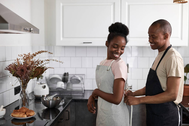 man helps woman to tie an apron in kitchen - Zdjęcie, obraz