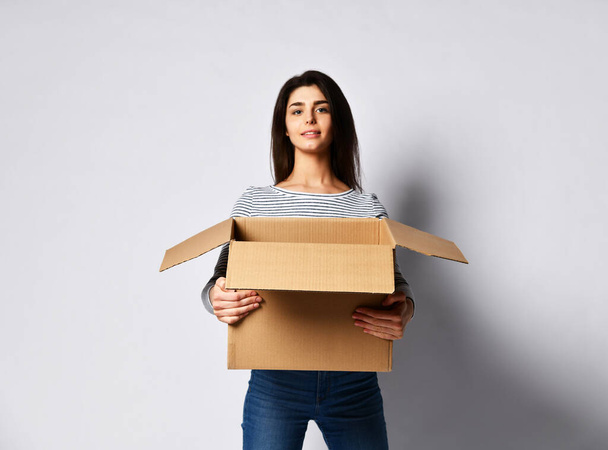 beautiful brunette woman standing on a light background with a moving cardboard box - Photo, image