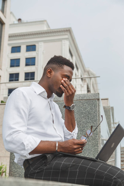 Ich fühle mich erschöpft. Frustrierter junger schwarzafrikanischer Mann hält die Augen geschlossen und sieht müde aus von der zusätzlichen Arbeit am Laptop - Foto, Bild