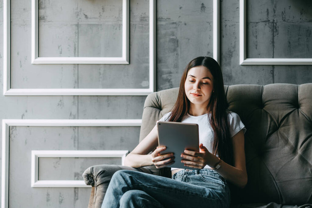 Beautiful young caucasian woman sitting on a sofa and using tablet computer. Work at home. High quality photo - Φωτογραφία, εικόνα