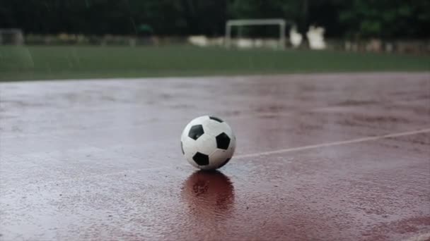 Nahaufnahme eines Fußballballs, der bei starkem Regen auf dem Laufband des Stadions vor dem Hintergrund eines Fußballtores liegt. Die Kamera ändert den Fokus - Filmmaterial, Video