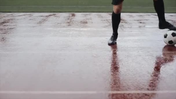 Fotbalový hráč v tréninku pláštěnky a kopne do míče v dešti. Kamera se pohybuje zdola nahoru. Detailní záběr - Záběry, video