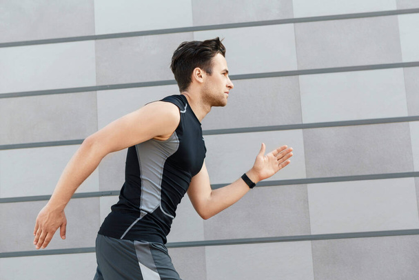 Jogging in morning. Handsome guy in sportswear and with fitness tracker, runs - Foto, Imagen