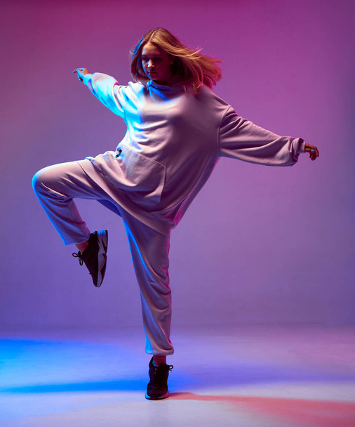 Stylish young girl, cool dancing in a hoodie with developing hair, on a neon background. Dance school poster - Photo, Image