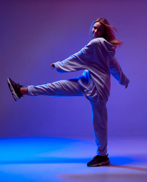 Stylish young girl, cool dancing in a hoodie with developing hair, on a neon background. Dance school poster - Fotografie, Obrázek