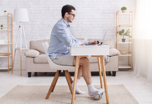 Sport, video conference and work from home. Businessman in shirt and shorts, sits at table and chatting, put foot on dumbbell - Foto, Imagen
