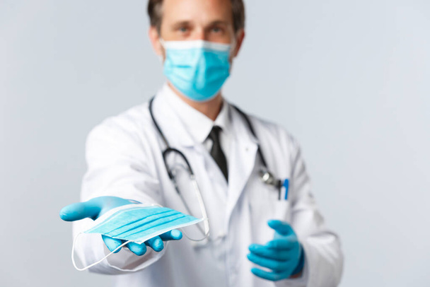 Covid-19, virus, gezondheidswerkers en vaccinatie concept. Dokter in PPE overhandigt u medisch masker, leggen preventieve maatregelen niet vangen coronavirus ziekte, zorgen patiënt gezondheid - Foto, afbeelding