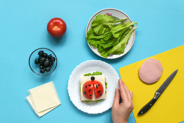 Funny sandwich for children in form of ladybug made of fresh tomato, salad, cheese, sausage, bacon and bread on blue background. Instruction how to make creative food art breakfast for kids. Step 6. - Фото, зображення