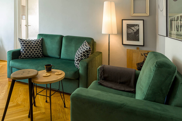 İçi koyu yeşil kanepe ve koltuk, lambanın yanında, masa ve tabure, yerde ahşap zemin. - Fotoğraf, Görsel