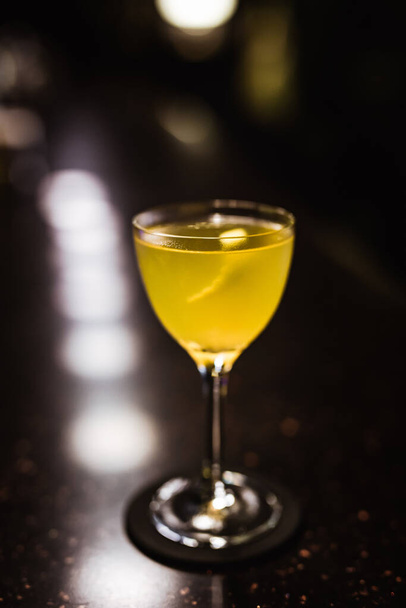A sour cocktail in a nick and nora glass in a dark and moody atmosphere of a bar - Photo, Image