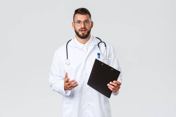 Terveydenhuollon työntekijät, sairausvakuutus ja covid-19 käsite. Ammattimainen nuori latino lääkäri lasit ja valkoinen takki, selittää potilaille tärkeitä info coronavirus, pidä leikepöydälle, puhua sinulle - Valokuva, kuva