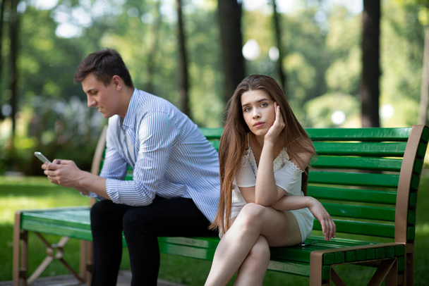 Sıkıcı randevularda sıkılmış genç bir kadın, erkek arkadaşları tarafından ihmal edilmiş ya da parkta akıllı telefon bağımlılığından muzdarip. - Fotoğraf, Görsel
