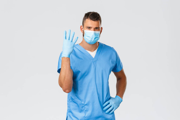 Healthcare workers, covid-19, coronavirus and preventing virus concept. Serious concerned doctor or nurse in scrubs, medical mask and gloves showing number four, give rules or important pandemic info - Foto, Imagem