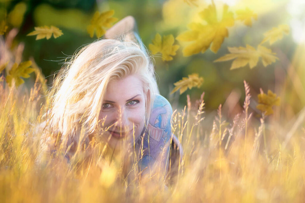 Mujer rubia bonita con tatuajes en la hierba de otoño
 - Foto, imagen