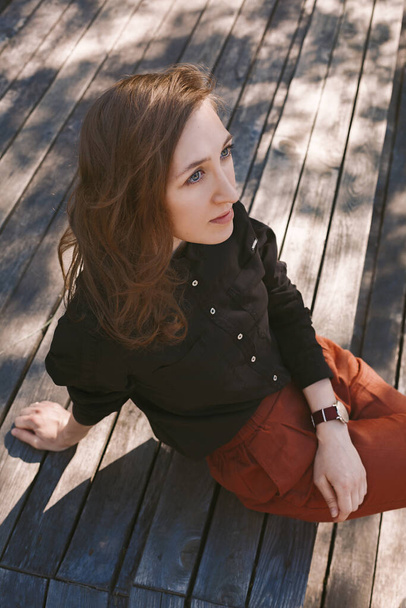 Brown-haired girl sitting on a wood boards awaiting for someone on sunny day - Photo, Image