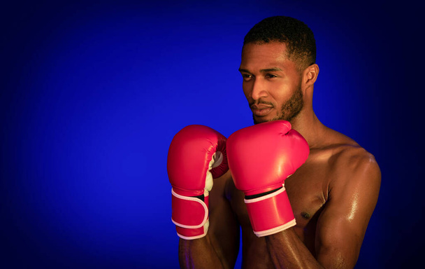 Profesionální boxer bez košile stojící v pozici připravené k boji na modrém pozadí - Fotografie, Obrázek