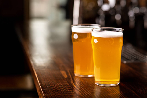 Kylmiä herkullisia juomia. Kaksi lasillista kevyttä olutta puisessa baaritiskillä pubissa - Valokuva, kuva