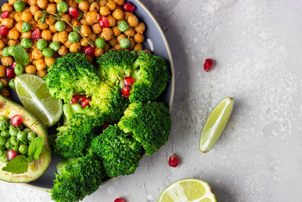 Healthy vegetable lunch of broccoli, roasted chickpeas, avocado, green peas, pomegranate seeds, lime and mint on a ceramic plate. Vegan food, clean eating or dieting concept. - Fotoğraf, Görsel