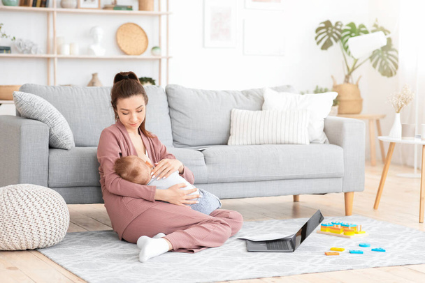 Caring Mom Nursing Baby While Working With LAptop And PApers At Home - Photo, Image