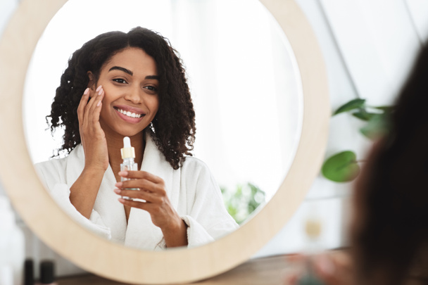 Skin Hydration. Positive black woman applying moisturizing serum on face - Fotografie, Obrázek