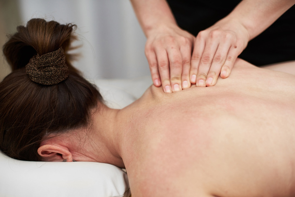 Vrouwelijke therapeut masseert een jonge vrouw op haar rug en schouders. Ontspannende massage. Therapeutische massage. Alternatieve geneeskunde. Kuuroorden. - Foto, afbeelding