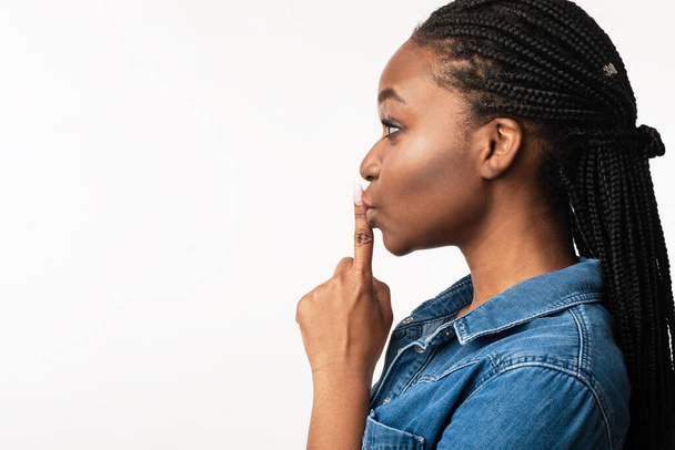 Femme noire gesticulant doigt sur les lèvres signe, fond blanc, vue de côté - Photo, image