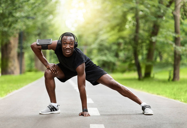 Sportos fekete srác nyújtózkodó test edzés előtt a parkban - Fotó, kép