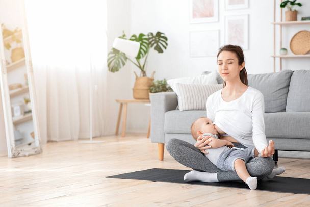 Χαλαρωμένη νεαρή μητέρα διαλογισμό, ενώ θηλάζει το μωρό της στο σπίτι, Εξάσκηση γιόγκα - Φωτογραφία, εικόνα