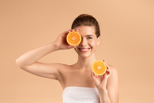 Disintossicazione naturale della pelle. Radiosa ragazza che tiene fette di arancia fresca su sfondo beige - Foto, immagini