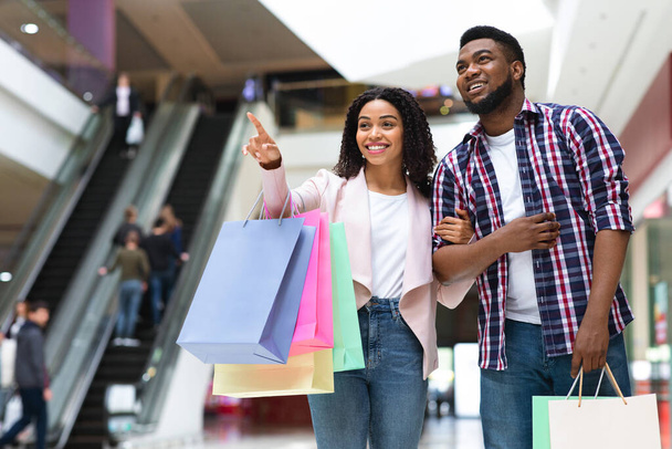 Birlikte alışveriş yapmak. Siyah kadın alışveriş merkezinde bir şeyi işaret ediyor, erkek arkadaşına gösteriyor. - Fotoğraf, Görsel