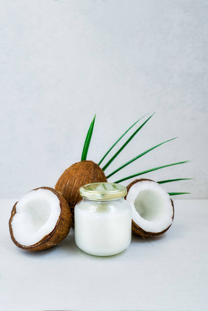 Fresh, healthy vegan plant based coconut butter jar with whole nuts and pulm leaf on the white marble background. Natural coconut oil for cooking and skincare. Selective focus. Vertical. Copy space - Photo, Image