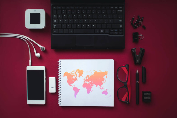 ノートパソコン、ヘッドフォン、世界地図のあるノートブックの上に黒い画面のスマートフォンで自宅のオフィスの机のワークスペース。コピースペース、フラットレイ付きのトップビュー - 写真・画像