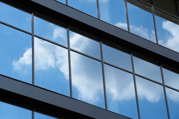 Parlak güneşli bir günde modern bir binanın ön cephesi, mavi gökyüzü ve bulutlar yansıyor yeni binanın güzel dış görünüşü. - Fotoğraf, Görsel