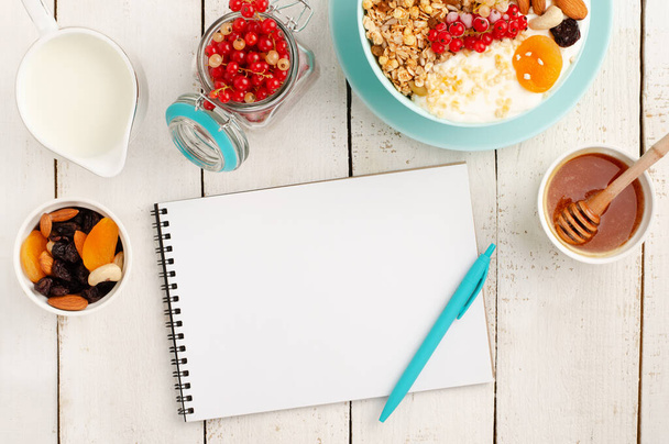 Notepad for weight loss plan, healthy breakfast of granola bowl on white wooden background. Top view - Photo, Image