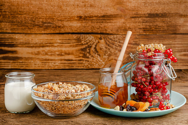 Granola casera con grosellas rojas frescas, leche y miel sobre fondo de madera. Comer sano, copiar espacio
 - Foto, Imagen