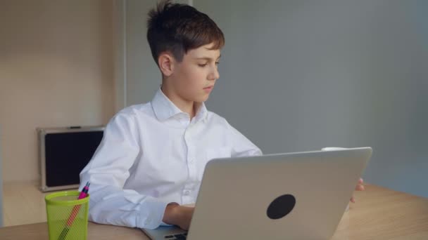 Bonito menino jovem empresário trabalhar em um laptop em casa e beber café. Aprendizagem online, lição à distância, educação em casa. Criança usando computador portátil
. - Filmagem, Vídeo