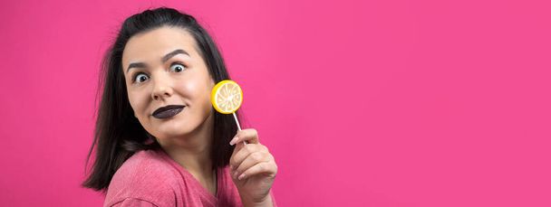 Portrait of lovely sweet beautiful cheerful woman with straight brown hair holding a lollipop near the eyes. - Photo, Image
