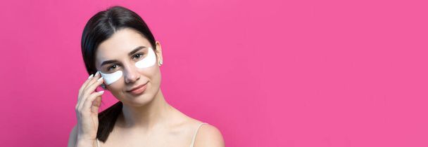 Κοντινό πορτραίτο όμορφου κοριτσιού με γυμνούς ώμους χρησιμοποιώντας μπαλώματα κάτω από τα μάτια. Μόνιμη πάνω από ροζ φόντο. - Φωτογραφία, εικόνα