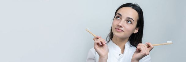 Una giovane ragazza bruna tiene in mano uno spazzolino ecologico. Una ragazza con un camice bianco promuove zero sprechi
. - Foto, immagini