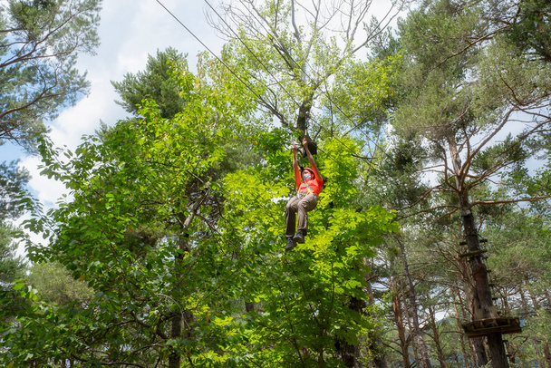 woman with facial mask jumping on a zip line in a pine forest - Foto, Bild